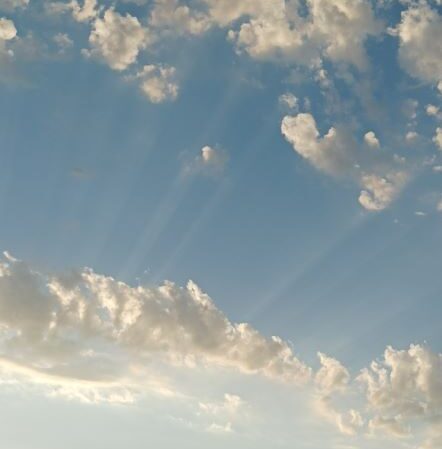 Rayons de soleil traversant des nuages doux dans un ciel bleu clair, symbolisant la guidance et la lumière intérieure.
